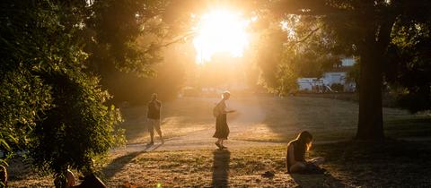 Die Abendsonne bescheint einen der trockenen, staubigen Wege im Frankfurter Günthersburgpark, der trotz der Hitze zum Abendspaziergang oder zum Verweilen einlädt. 