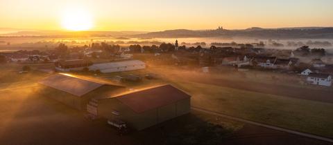 Beim Sonnenaufgang zieht Nebel über Felder und Stadt