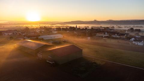 Beim Sonnenaufgang zieht Nebel über Felder und Stadt