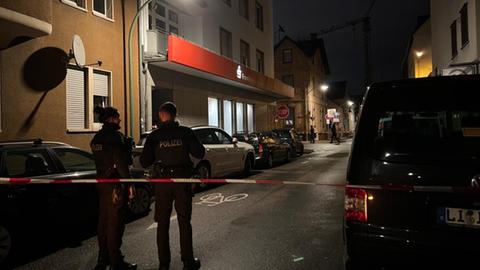 Tatort vor einer Bankfiliale in Frankfurt-Griesheim, in der nachts ein Geldautomat gesprengt wurde. Eine Polizeiabsperrung, dahinter stehen zwei Polizisten. 