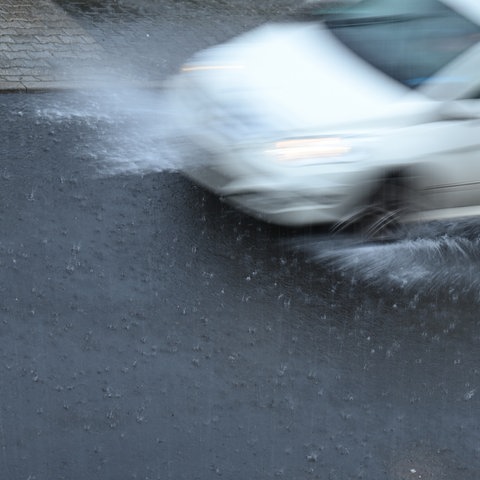 Ein Auto ist bei Starkregen auf einer Straße unterwegs.  