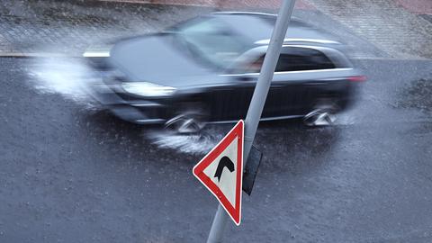 Dunkles Auto fährt durch hochstehendes Regenwasser auf der Strasse, es spritzt