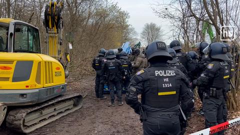 Polizisten stehen neben einem Bagger im Fechenheimer Wald.