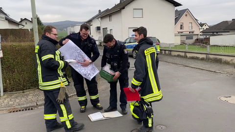 Feuerwehrleute laufen hinter einer Absperrung zu einem Wohnhaus. 