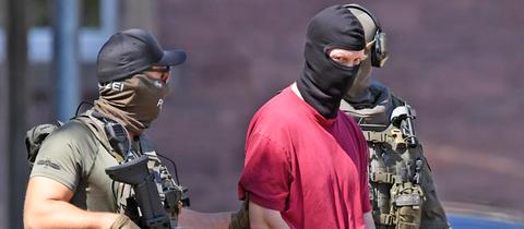 Stephan E. mit Handschellen und Gesichtsmaske scharf bewacht von bewaffneten Polizisten auf dem Weg zu einem Hubschrauber