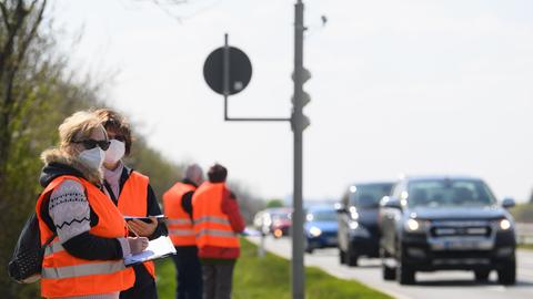 Verkehrszählerinnen stehen an einer Straße und tragen vorbeifahrende Autos nach Typ in eine Liste ein.