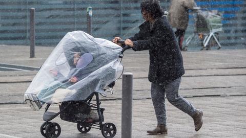 Eine Frau schiebt einen Kinderwagen mit Regenschutz durch den aufgepeitschten Regen.