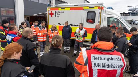 Einsatzkräfte stehen bei einer Lagebesprechung neben einem Fahrzeug des Deutschen Roten Kreuzes.
