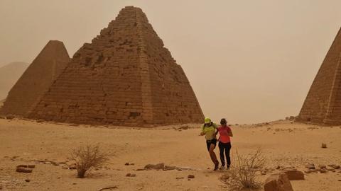 Zwei Menschen laufen an Pyramiden vorbei.