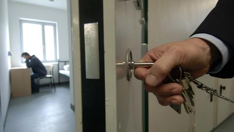 Halb geöffnete Gefängniszelle - Schlüssel in der Hand eines Justizbeamten, steckt im Schloss.