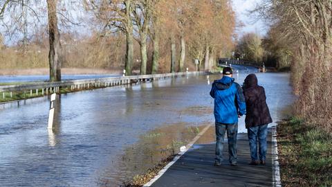 Zwei Spaziergänger stehen an einer überfluteten Landstraße bei Heuchelheim (Gießen).