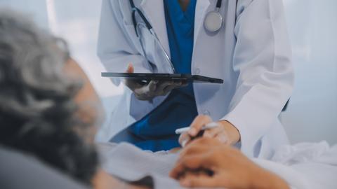 Patientin liegt im Bett und wird von Person in weißem Kittel versorgt