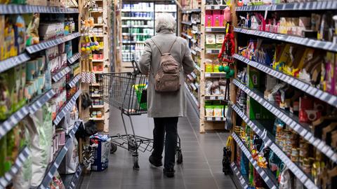 Eine Frau geht mit ihrem Einkaufswagen durch einen Supermarkt.