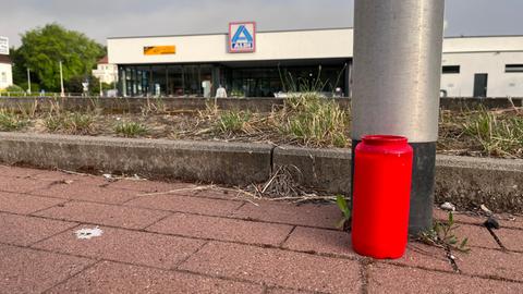 Ein Grablicht steht vor einer Laterne auf dem Parkplatz des Supermarkts, der im Hintergrund noch zu erkennen ist.