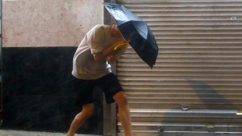 Ein Mann mit einem Regenschirm läuft auf einer Straße und kämpft gegen den starken Wind und den Regen.
