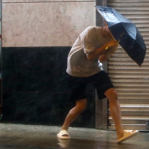 Ein Mann mit einem Regenschirm läuft auf einer Straße und kämpft gegen den starken Wind und den Regen.