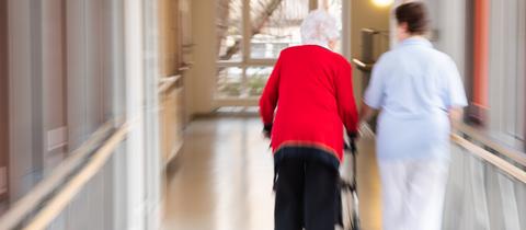 Eine Pflegerin läuft Seite an Seite mit einer älteren Bewohnerin durch den Flur eines Altenpflegeheims. (dpa)