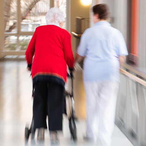 Eine Pflegerin läuft Seite an Seite mit einer älteren Bewohnerin durch den Flur eines Altenpflegeheims. (dpa)
