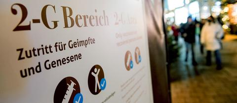 Ein Schild mit der Aufschrift "2-G Bereich, Zutritt für Geimpfte und Genesene". In Hintergrund ist unscharfn ein Weihnachtsmarkt zu sehen. 