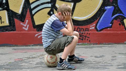 Ein Junge sitzt auf einem Ball und hält sich die Hände vor das Gesicht.