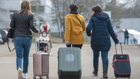 Drei Frauen gehen mit Rollkoffern in der Hand eine Straße entlang.