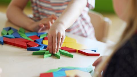 Kinderhände, die an einem Tisch mit blauen, gelben und roten Holzelementen spielen.