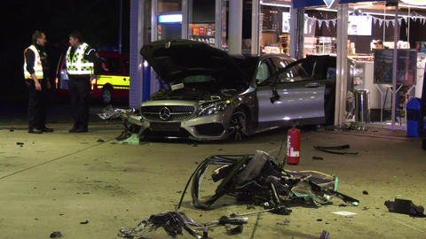 Ein beschädigtes Auto steht auf dem Hof einer Tankstelle.