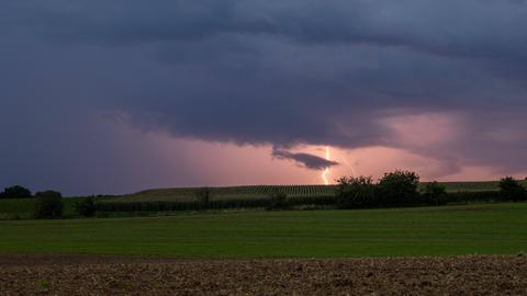 Über Feldern und Wiesen zieht eine Gewitterfront, ein Blitz schlägt in der Ferne ein.