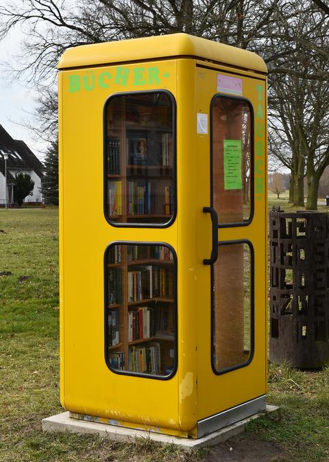 Bücherregale stehen in einer gelben Telefonzelle.