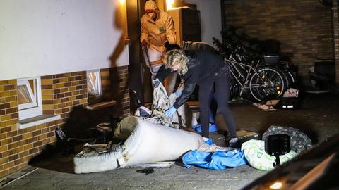 Eine Polizistin durchsucht verbrannte Überreste von Einrichtungsgegenständen vor einem Wohnhaus in Rodgau.