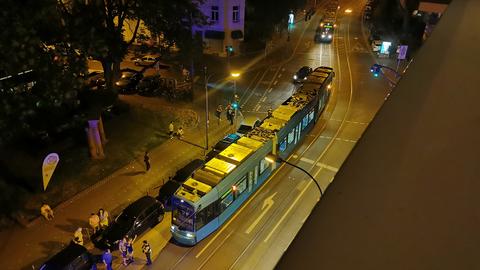 Eine grüne Straßenbahn steht auf einer Straße, davor eine Gruppe von Menschen.