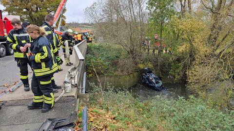 Rettungskräfte an der unfallstelle, kaputtes Auto im Fluss