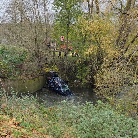 Rettungskräfte an der unfallstelle, kaputtes Auto im Fluss