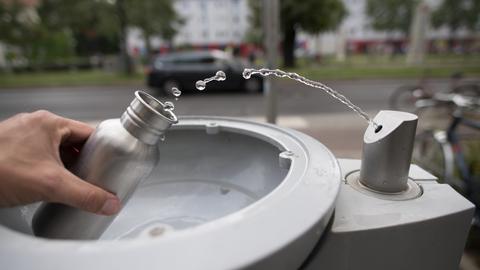 An einem Wasserspender der Berliner Wasserbetriebe füllt sich ein Passant seine Trinkflasche mit Wasser auf. 