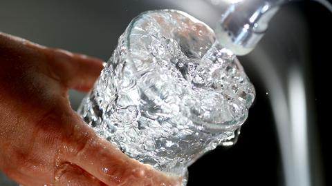 Wasser fließt aus einem Wasserhahn in ein Glas.