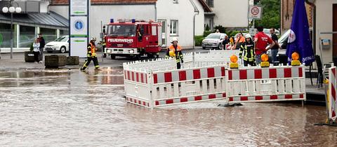 Braunes Wasser steht in einer Straße, darin und daneben Mitarbeitende und Autos der Feuerwehr.