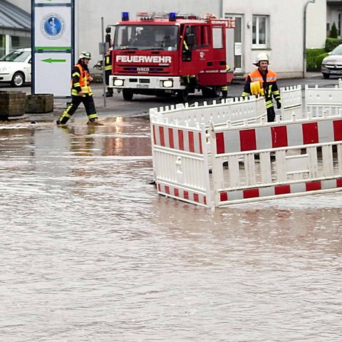 Braunes Wasser steht in einer Straße, darin und daneben Mitarbeitende und Autos der Feuerwehr.