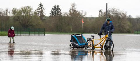 Ein Mann schiebt sein Fahrrad über eine Straße, die voller Wasser ist.