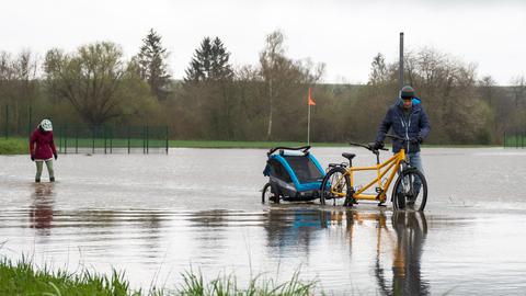 Ein Mann schiebt sein Fahrrad über eine Straße, die voller Wasser ist.