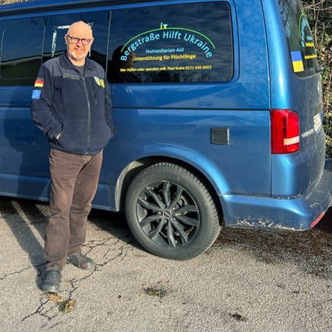 Ein Mann steht vor einem Auto, auf dem steht "Bergstraße hilft Ukraine", und schaut in die Kamera.