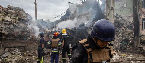 Feuerwehrleute stehen vor einem zerstörten Schulgebäude.