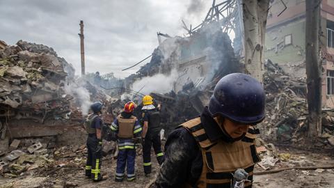 Feuerwehrleute stehen vor einem zerstörten Schulgebäude.