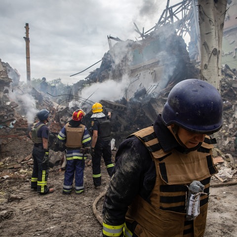 Feuerwehrleute stehen vor einem zerstörten Schulgebäude.