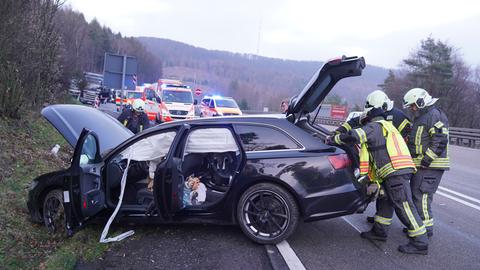 Zwei Feuerwehrleute stehen vor einem schwarzen Auto, dessen Motorhaube beschädigt ist.