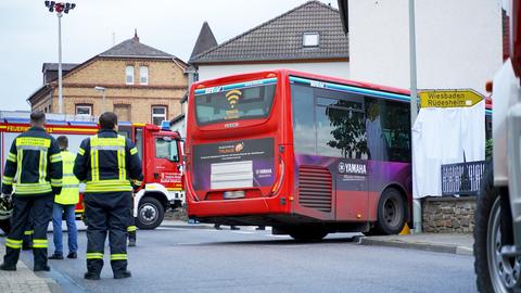 Auf einer Straße stehen Einsatzkräfte der Feuerwehr vor einem RMV-Linienbus, der an einer Straßenecke steht, und einem Feuerwehrauto.