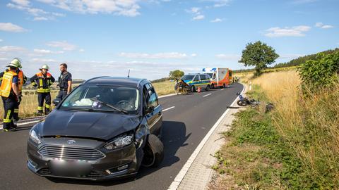 Der verunfallte Pkw steht auf der Straße, das verunfallte Motorrad liegt am Straßenrand.