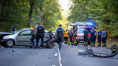 Einsatzkräfte stehen auf einer Bundesstraße um ein Autowrack herum.