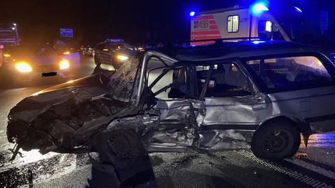 Ein zerbeultes Auto steht auf einer Straße, dahinter Wagen der Rettungskräfte