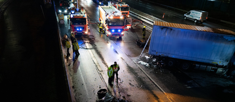 Ein Lkw steht nach einem Unfall quer auf einer Autobahn, daneben Trümmerteile, ein zerstörtes Auto und mehrere Einsatzfahrzeuge.