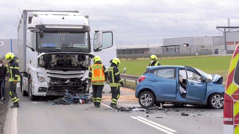 Unfallstelle: Auf einer Bundesstraße stehen Feuerwehrleute zwischen einem beschädigten Lkw und einem demolierten Kleinwagen. 